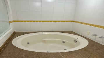 Een badkamer met een vrijstaand bad, witte betegelde wanden en een bruin granieten aanrechtblad.