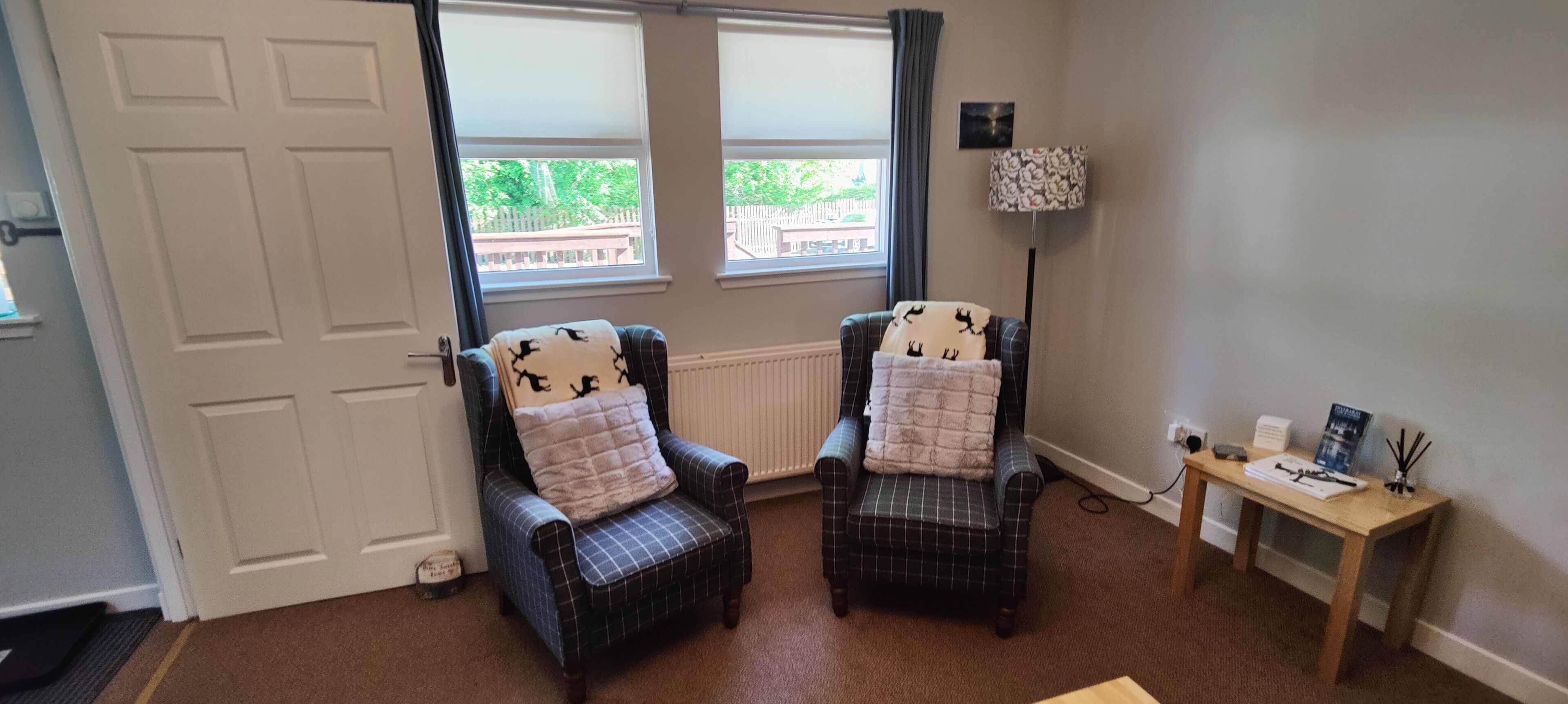 A room with two plaid armchairs, a small table with a lamp, and a view of a wooden deck outside.