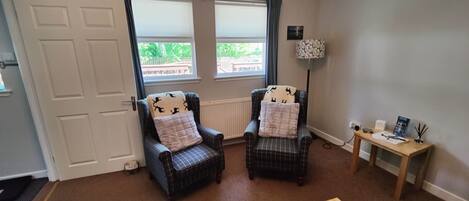 A room with two plaid armchairs, a small table with a lamp, and a view of a wooden deck outside.