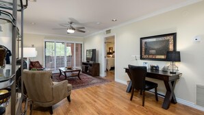 A spacious living room with a wooden floor, a ceiling fan, a TV, a dining area with a table and chairs, and a bedroom visible through an open door. - CASA DE LA VIDA - Anasazi Village - Golf View (Phoenix)