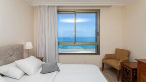 Ein Hotelzimmer mit Bett, Stuhl, Nachttisch und einem Fenster mit Meerblick.
