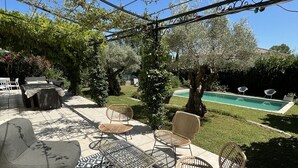 Patio esterno con piscina, zona salotto e pergolato ricoperto di piante rampicanti.