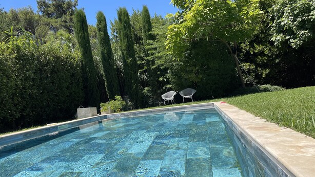 Una piscina rettangolare con acqua cristallina, circondata da un solarium in pietra e una zona verde.