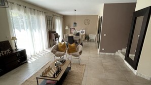 Un ampio soggiorno con una grande finestra, un'area pranzo con tavolo e sedie, e un angolo salotto accogliente con divano e poltrone.