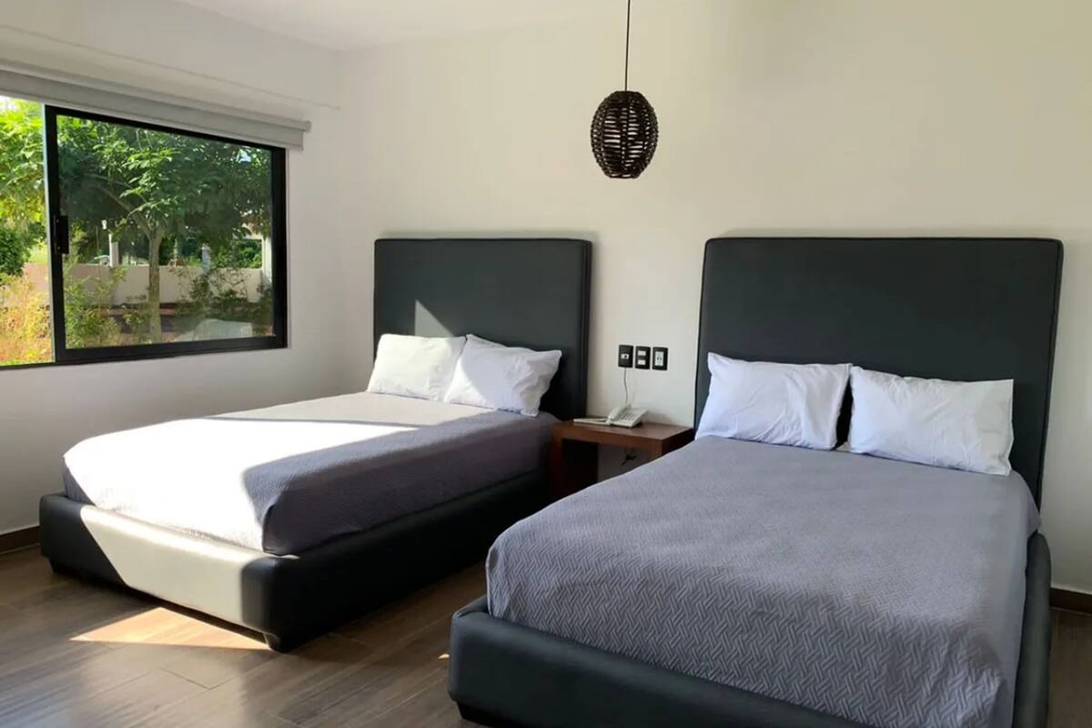 Habitación de hotel con dos camas, un ventanal grande y una lámpara colgante.