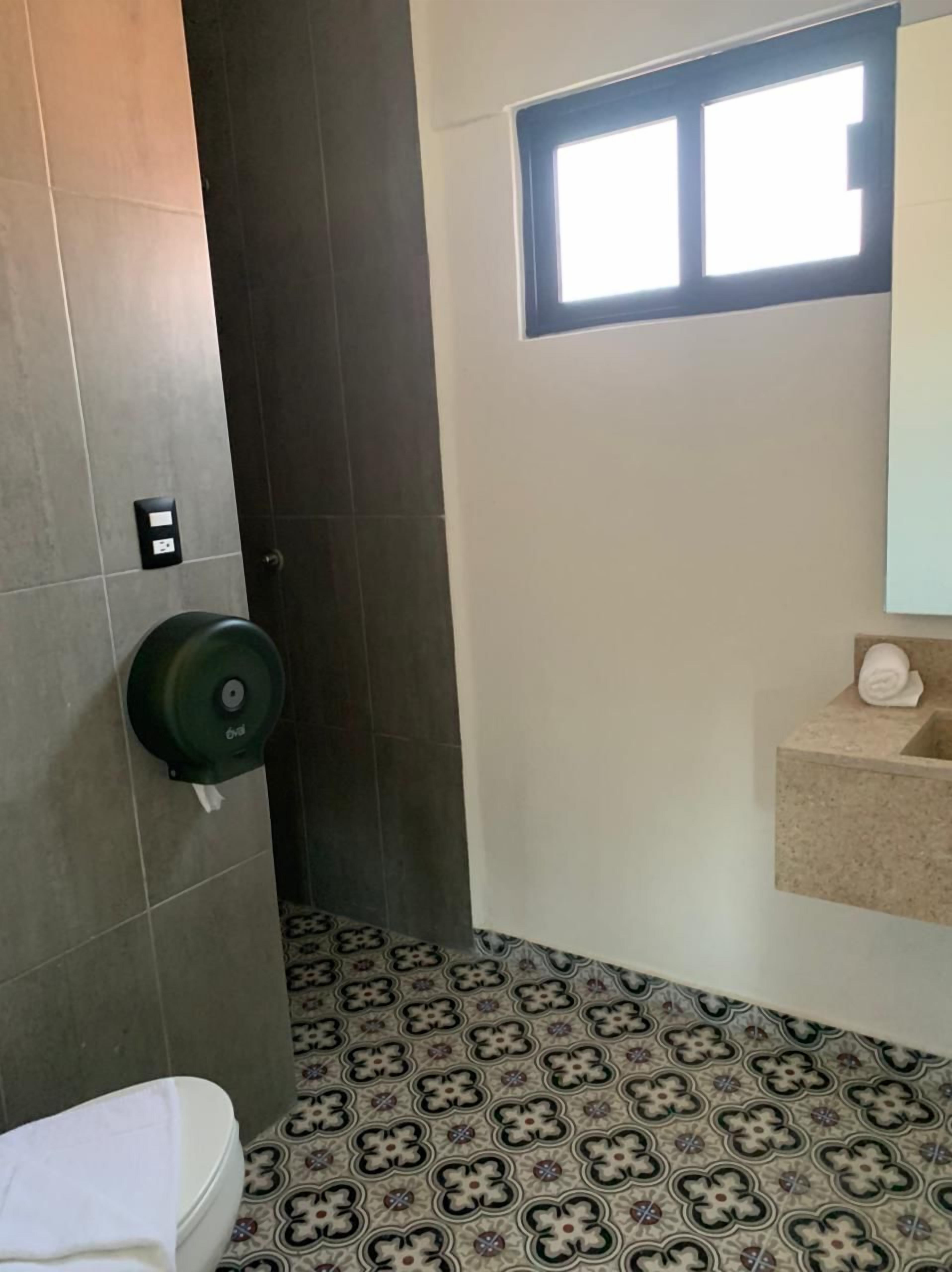 Een badkamer met een toilet, een zeepdispenser, een wastafel met spiegel en vloertegels met een patroon.