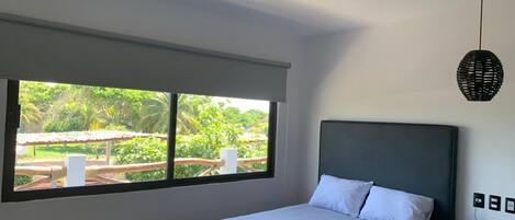 Un dormitorio con cama, mesita de noche, teléfono, ventilador de techo y ventana con vistas a zonas verdes.