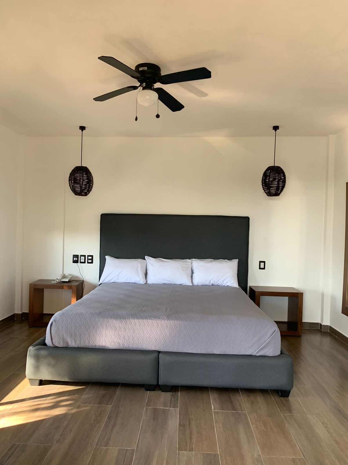 A modern bedroom with a large bed, two bedside tables, a ceiling fan, and two wall-mounted lamps.