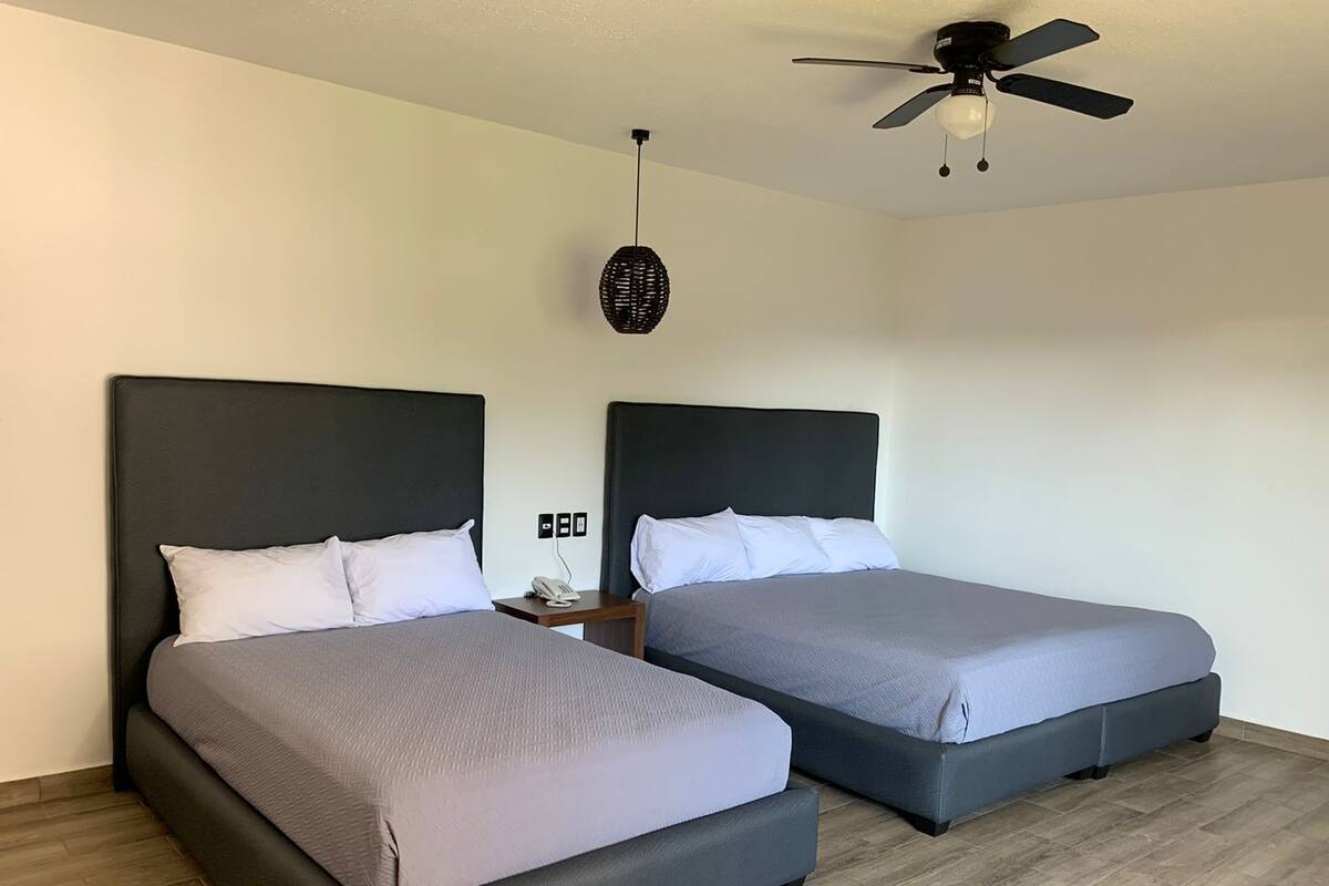 Habitación de hotel con dos camas, ventilador de techo, teléfono en la pared y un tapiz con textura.