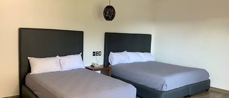 Habitación de hotel con dos camas, ventilador de techo, teléfono en la pared y un tapiz con textura.