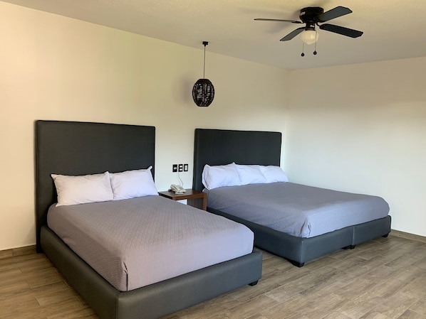 Habitación de hotel con dos camas, ventilador de techo, teléfono en la pared y un tapiz con textura.