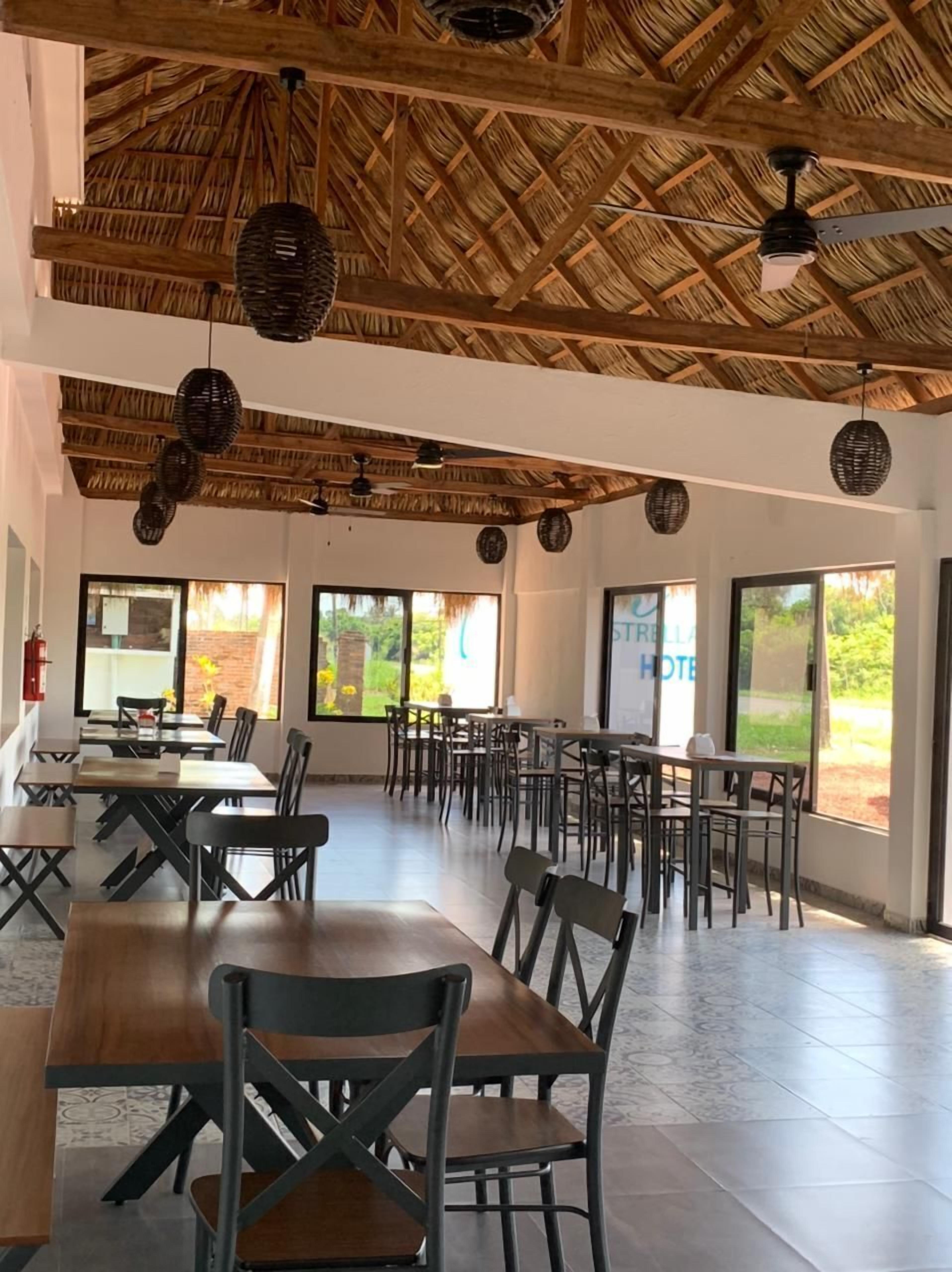 A spacious dining area with high ceilings, thatched roof, and large windows offering views of greenery.