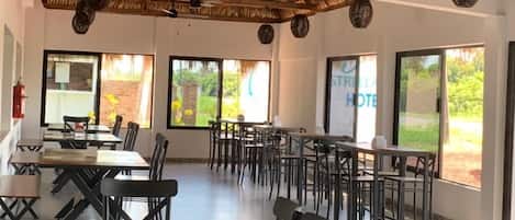 Un comedor amplio con techos altos, techo de paja y ventanas grandes que ofrecen vistas al verdor.