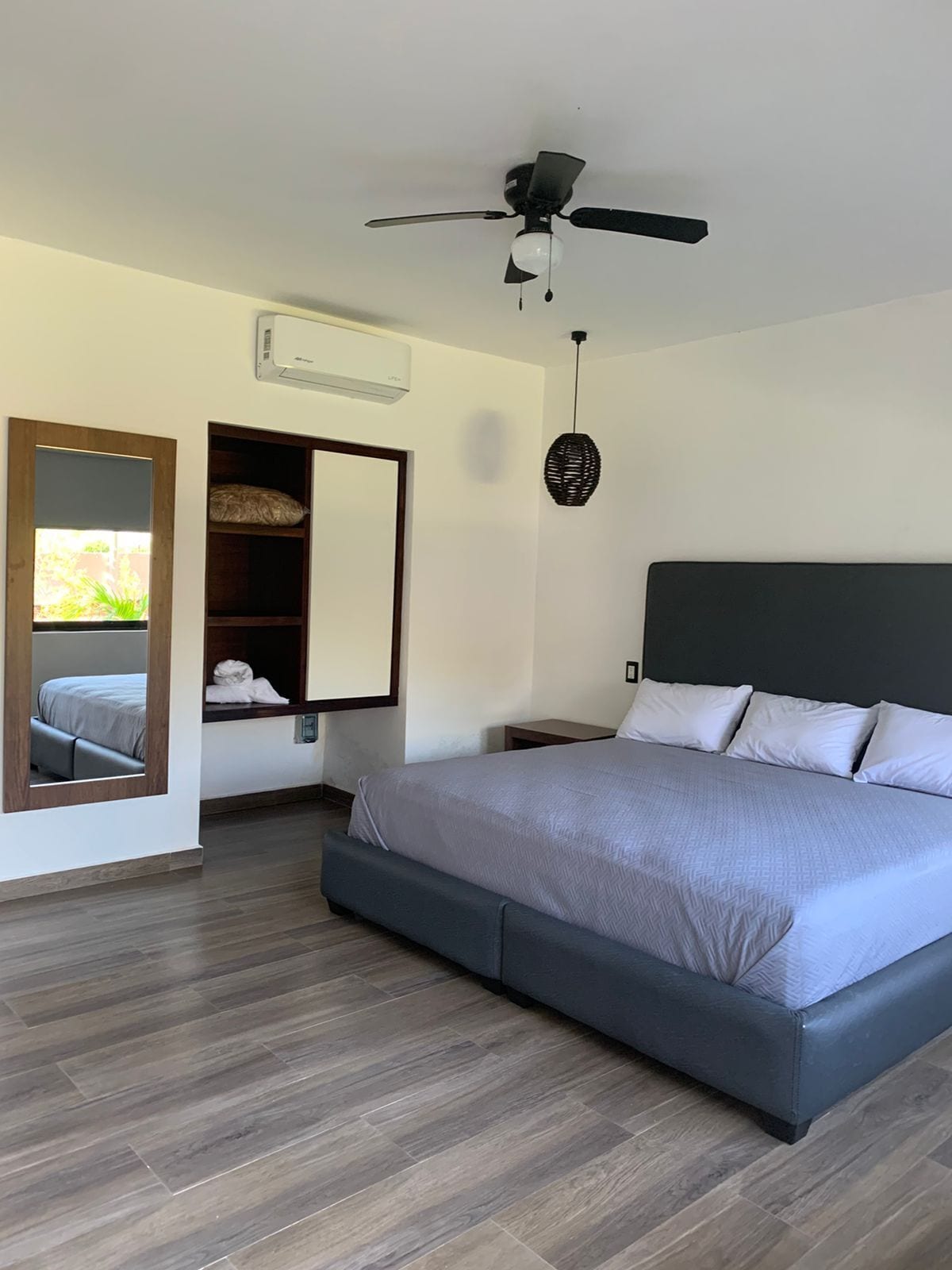 A modern bedroom with a large bed, a ceiling fan, a built-in wardrobe, and a mirror.