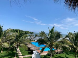 A pool area with palm trees, a thatched roof structure, and a view of the ocean. - Mar De Estrellas (Tecolutla)