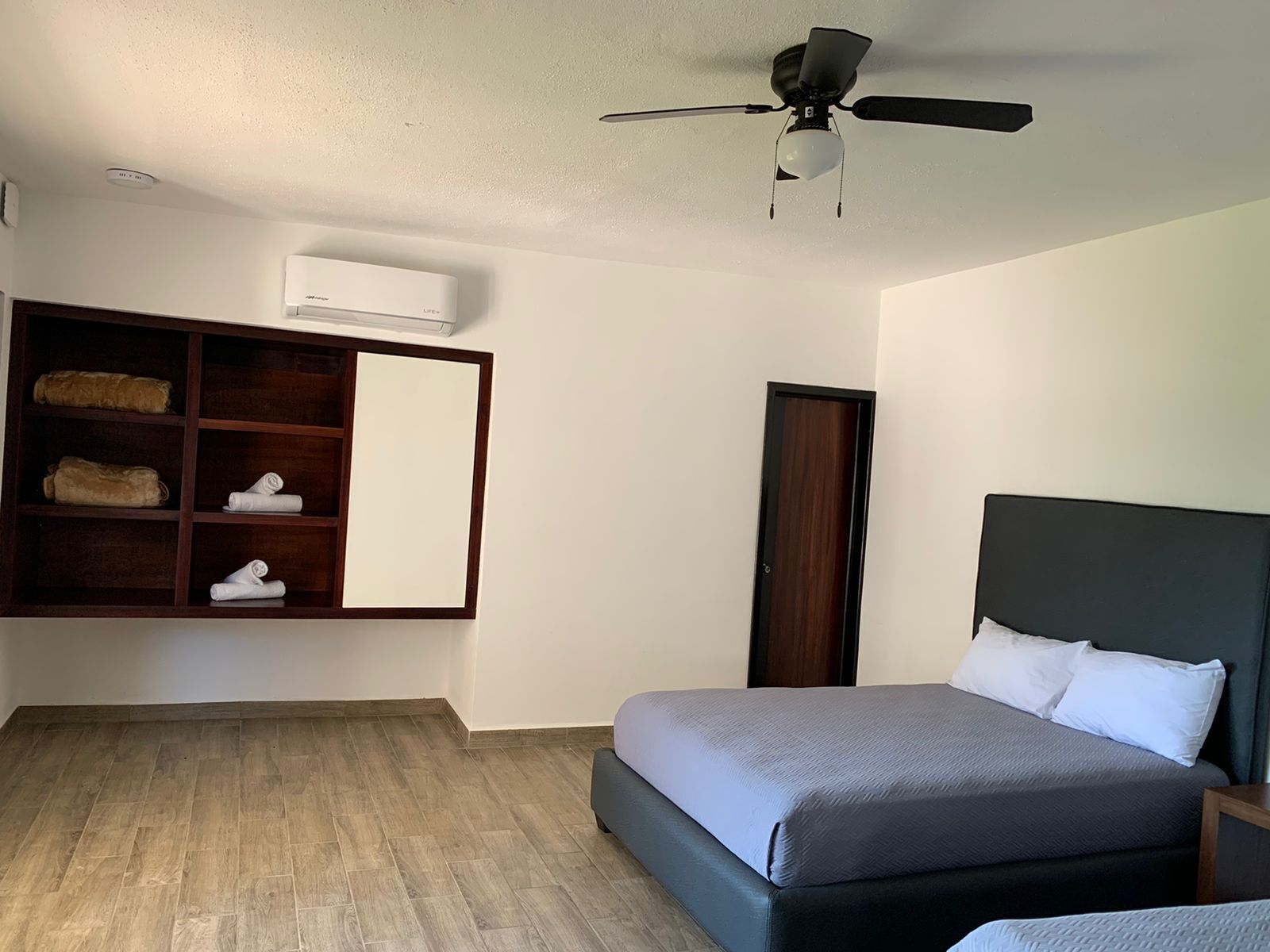 Un dormitorio con cama, ventilador de techo, armario y estante empotrado con toallas.