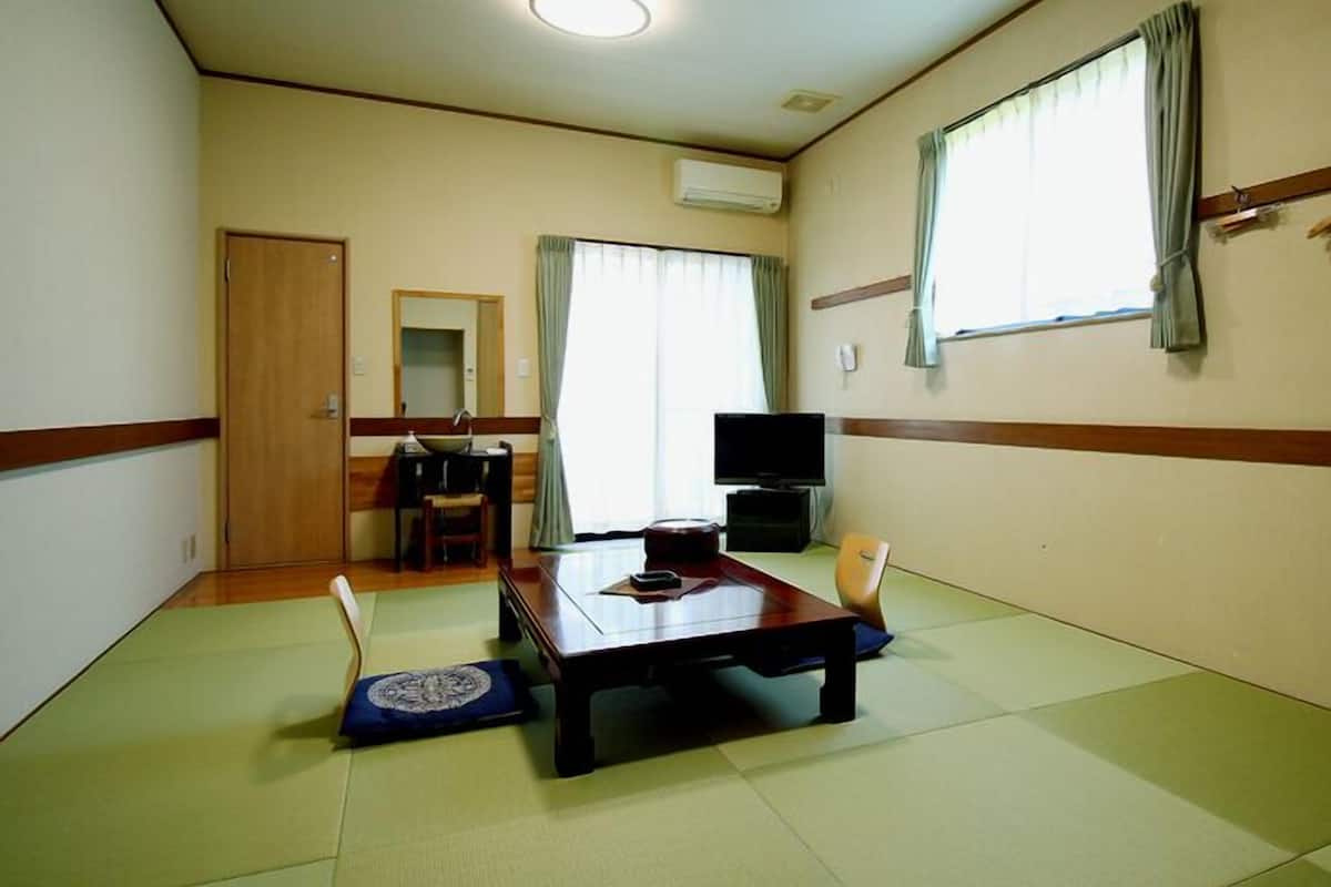 A hotel room with tatami mats, a wooden table, a television, a desk with a chair, and a wardrobe.