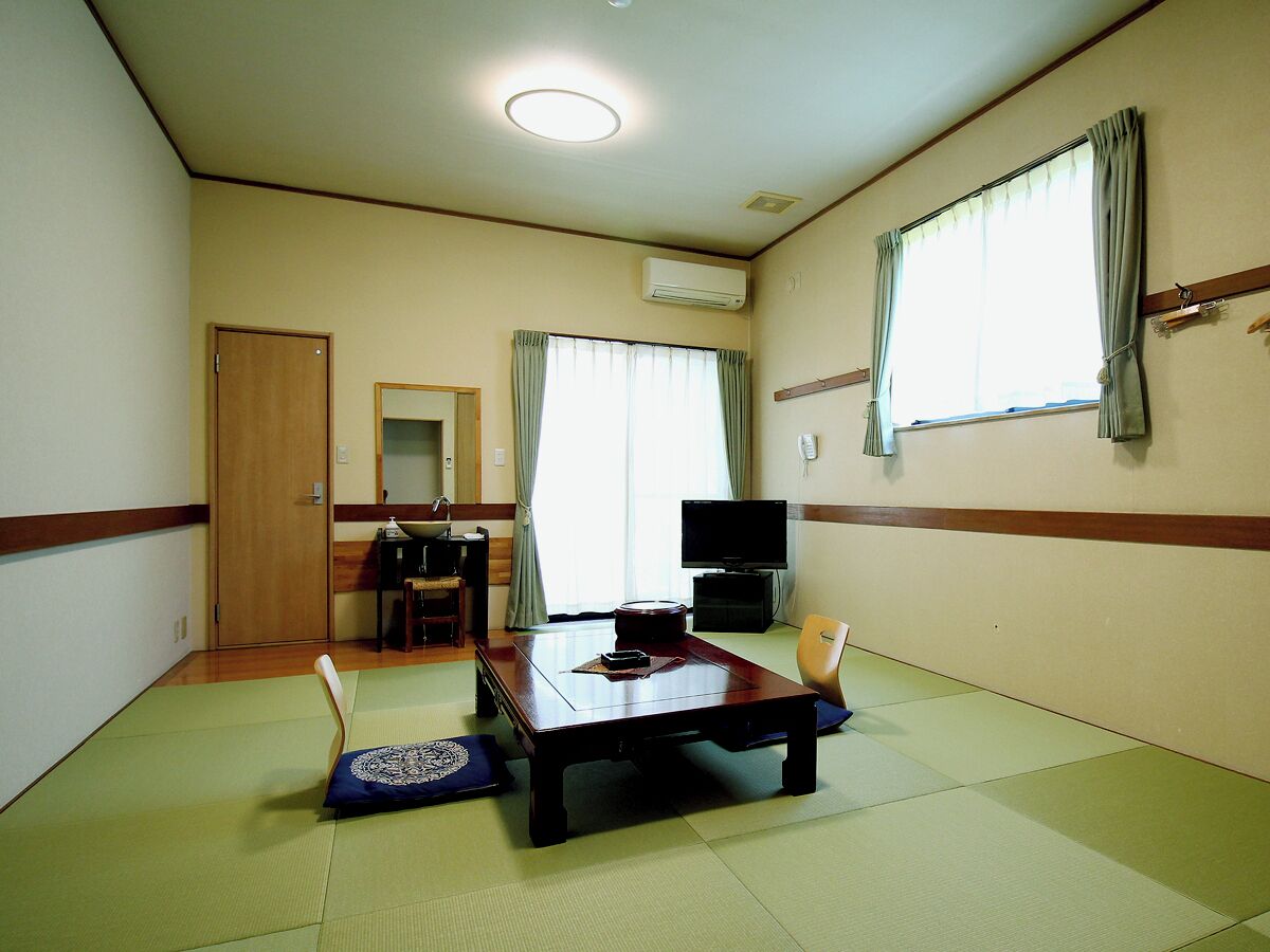 A room with tatami flooring, a wooden table, a television, and a sliding door.