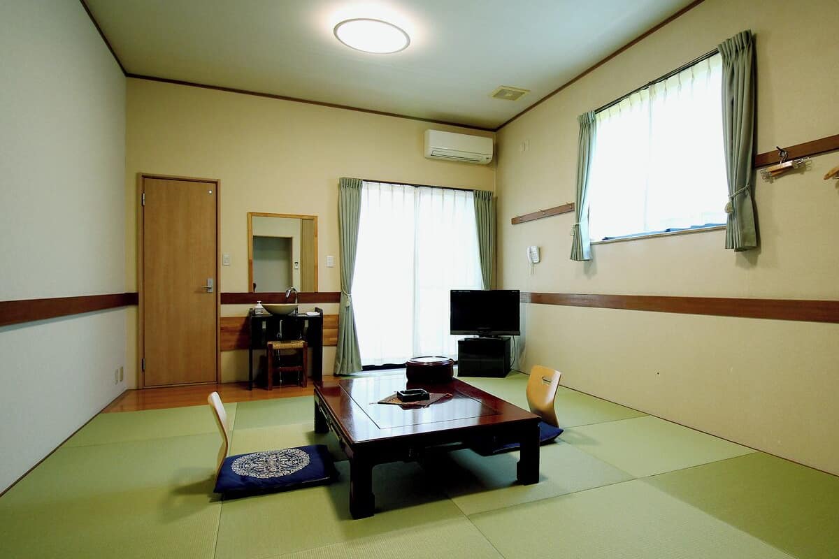 A room with tatami flooring, a wooden table, a television, and a sliding door.