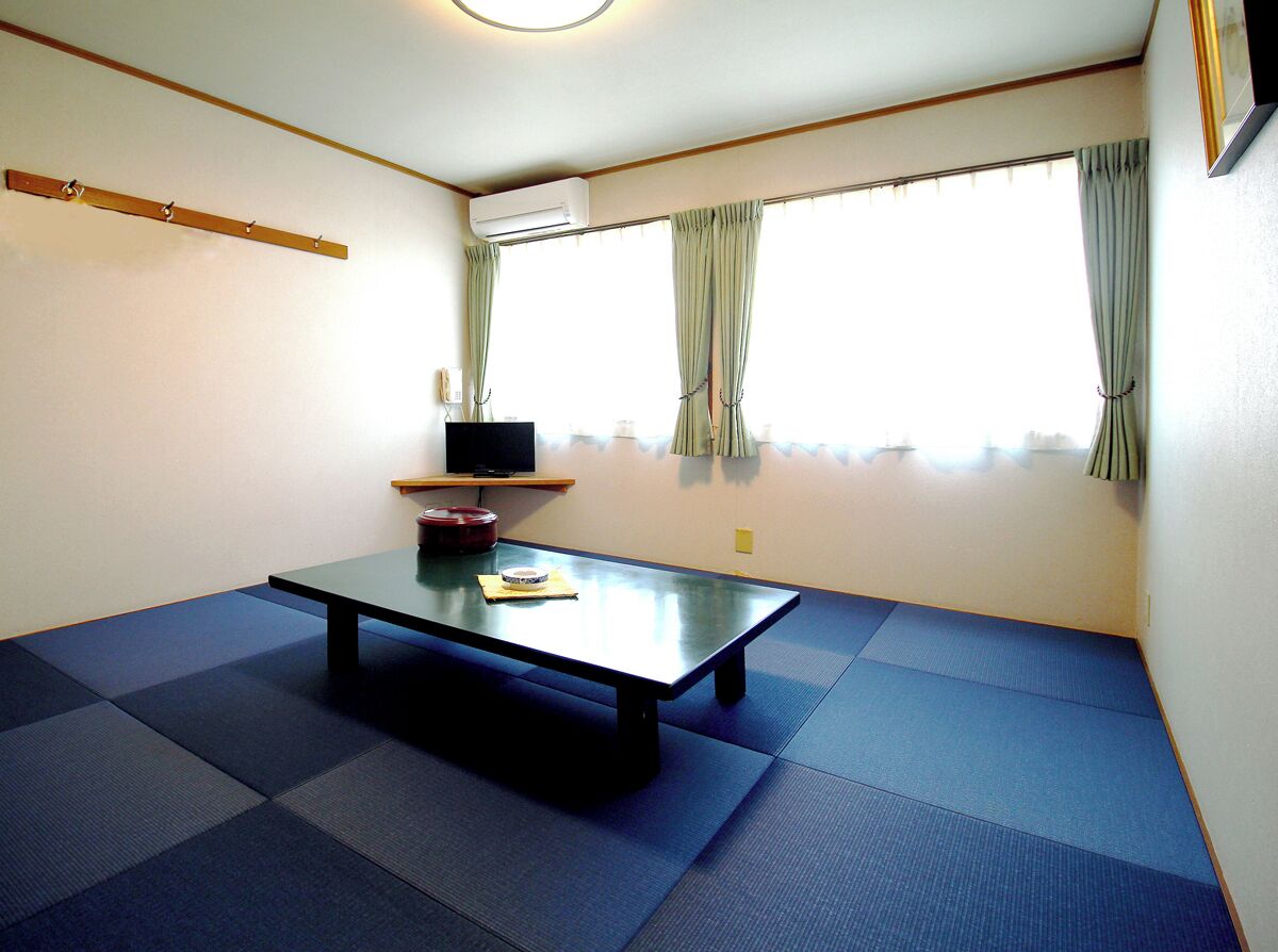 A room with tatami mat flooring, a low table with a laptop, and a window with curtains.