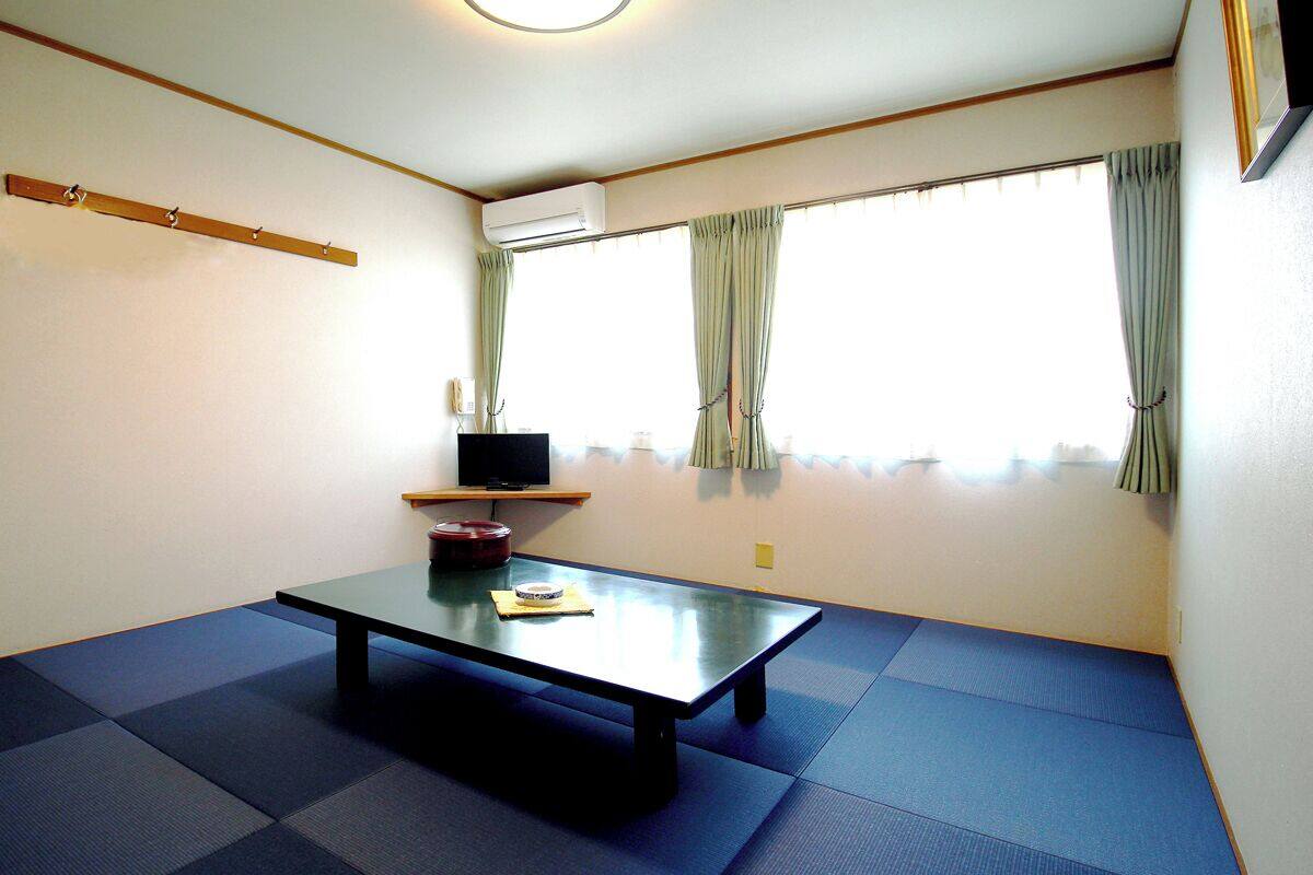 A room with tatami mat flooring, a low table with a laptop, and a window with curtains.