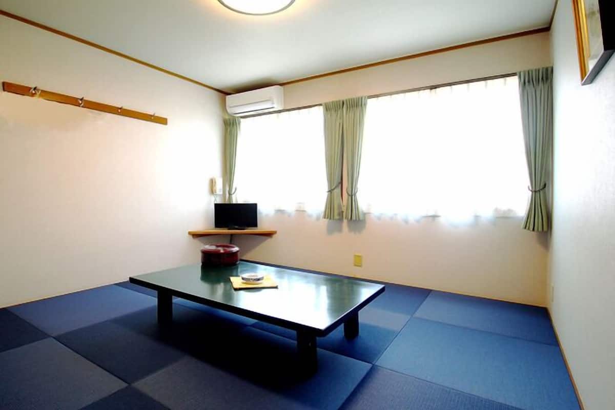 A room with tatami mat flooring, a low table, a television on a shelf, and a window with curtains.