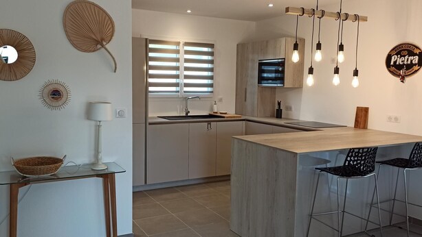Una cocina moderna con una isla central, taburetes de bar, un televisor y decoración en la pared.