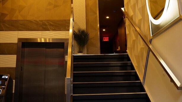 Un moderno vestíbulo de hotel con una escalera, un cajero automático y una lámpara decorativa en el techo.