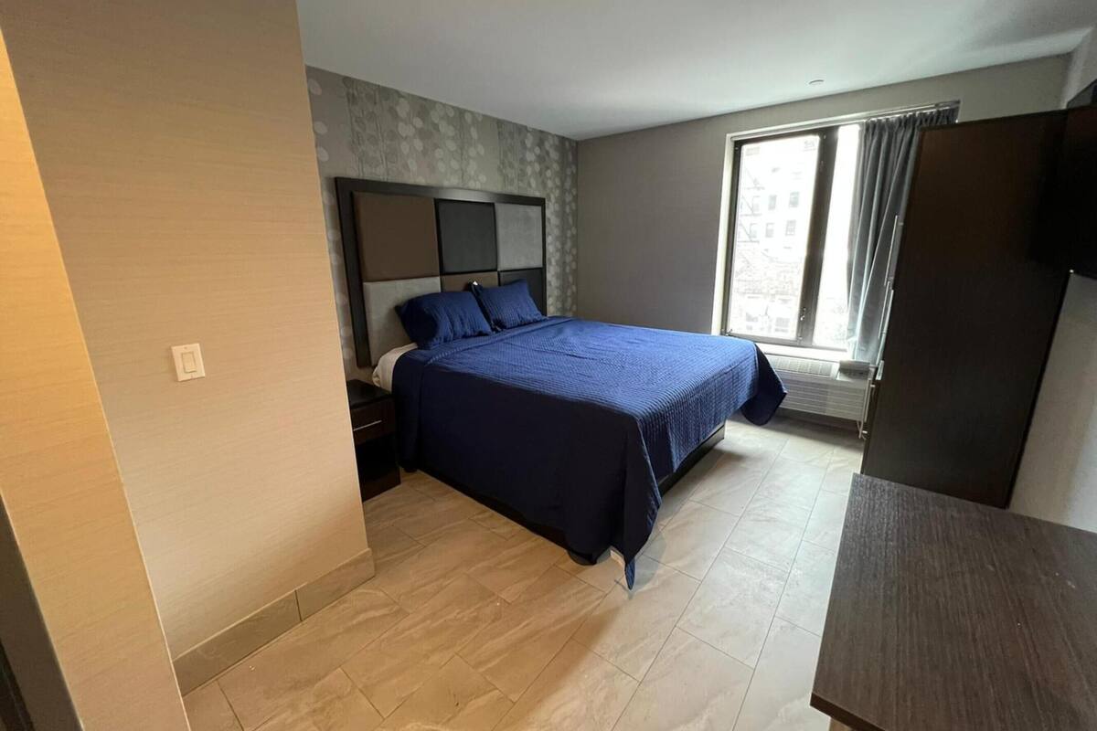 A bedroom with a bed, a nightstand, a window with curtains, and a wardrobe.