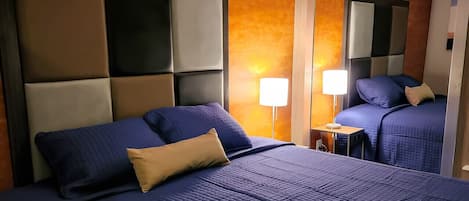 Habitación de hotel con una cama grande, una mesita de noche con una lámpara y un espejo que refleja la cama y la mesita.