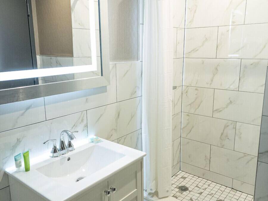 A bathroom with a white sink, mirror, and shower area with tiled walls.