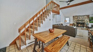 Un amplio salón con escalera de madera, chimenea de piedra y mesa con bancos.