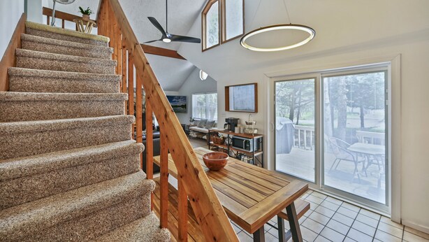 Una escalera con barandillas de madera conduce a un comedor con un gran ventanal y vistas al exterior.