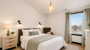A bedroom with a bed, bedside tables, a lamp, a window with curtains, and a view outside.
