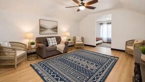 A living room with a sofa, two armchairs, a patterned rug, a ceiling fan, and a painting on the wall.