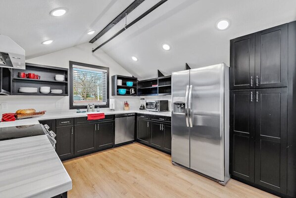 A modern kitchen with black cabinets, stainless steel appliances, and a wooden floor.