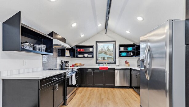 A modern kitchen with black cabinets, stainless steel appliances, and a wooden floor.