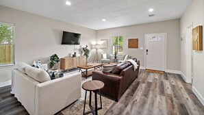 Ein modernes Wohnzimmer mit Sofa, Sessel, Couchtisch und Fernseher.