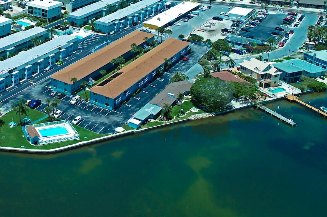 An aerial view of a coastal area with a large building, a parking lot, and a swimming pool.