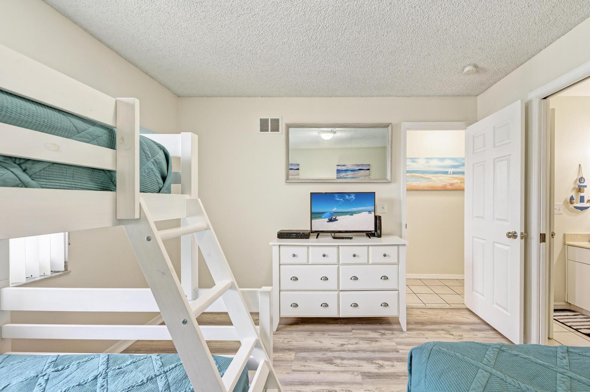A bedroom with bunk beds, a dresser, a television, and a door leading to another room.