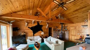 A log cabin interior with two white sofas, a wooden coffee table, a fireplace, and various mounted animal heads on the walls. - Quiet "UP NORTH" Cabin with all the Amenities. 200 a night. (Lakewood)