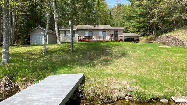 A single-story house with a garage, a deck, and a small pond. - Quiet "UP NORTH" Cabin with all the Amenities. 200 a night. (Lakewood)