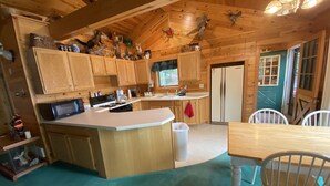 A wooden cabin kitchen with a central island, wooden cabinets, a refrigerator, and a dining area with a table and chairs. - Quiet "UP NORTH" Cabin with all the Amenities. 200 a night. (Lakewood)
