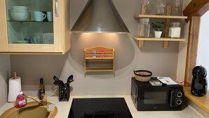 Una cocina con estufa, microondas y repisas con cristalería.