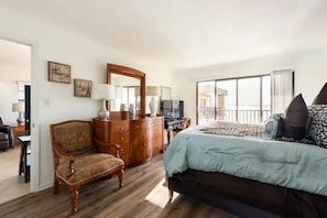 Une chambre avec un grand lit, une commode, une chaise et un bureau. Il y a une fenêtre donnant sur l’extérieur.
