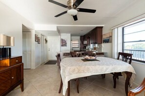 Un coin repas avec une table dressée pour quatre personnes, un ventilateur de plafond et une vue sur la cuisine et l’extérieur.