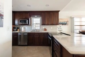 Una cocina con armarios de madera oscura, electrodomésticos de acero inoxidable y encimera de mármol blanco.