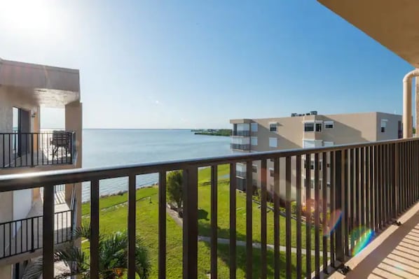 A balcony with a view of the sea, a grassy area, and a building with a modern design.