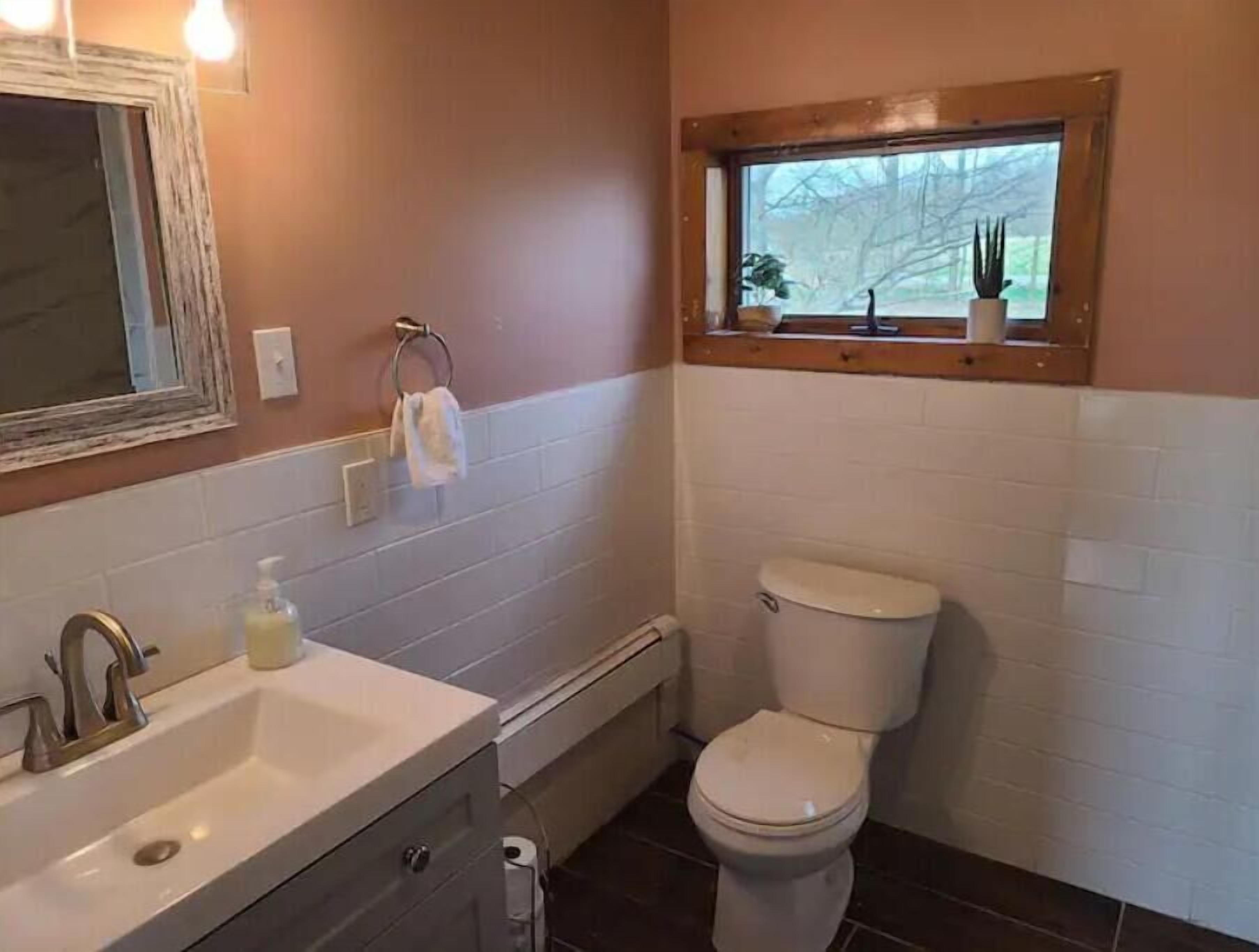 A bathroom with a sink, toilet, and a window above the toilet.