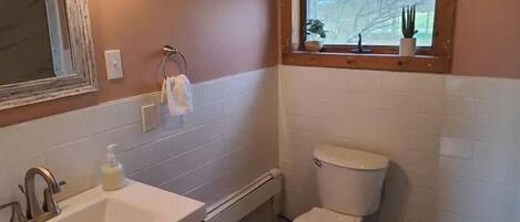 A bathroom with a sink, toilet, and a window above the toilet.